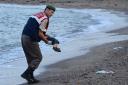 A Turkish police officer carries the body of Alan Kurdi off the shores in beach near Bodrum, southern Turkey