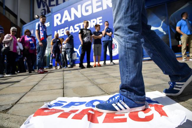 A Rangers fan stands on a Sports Direct banner during a protest at Ibrox.