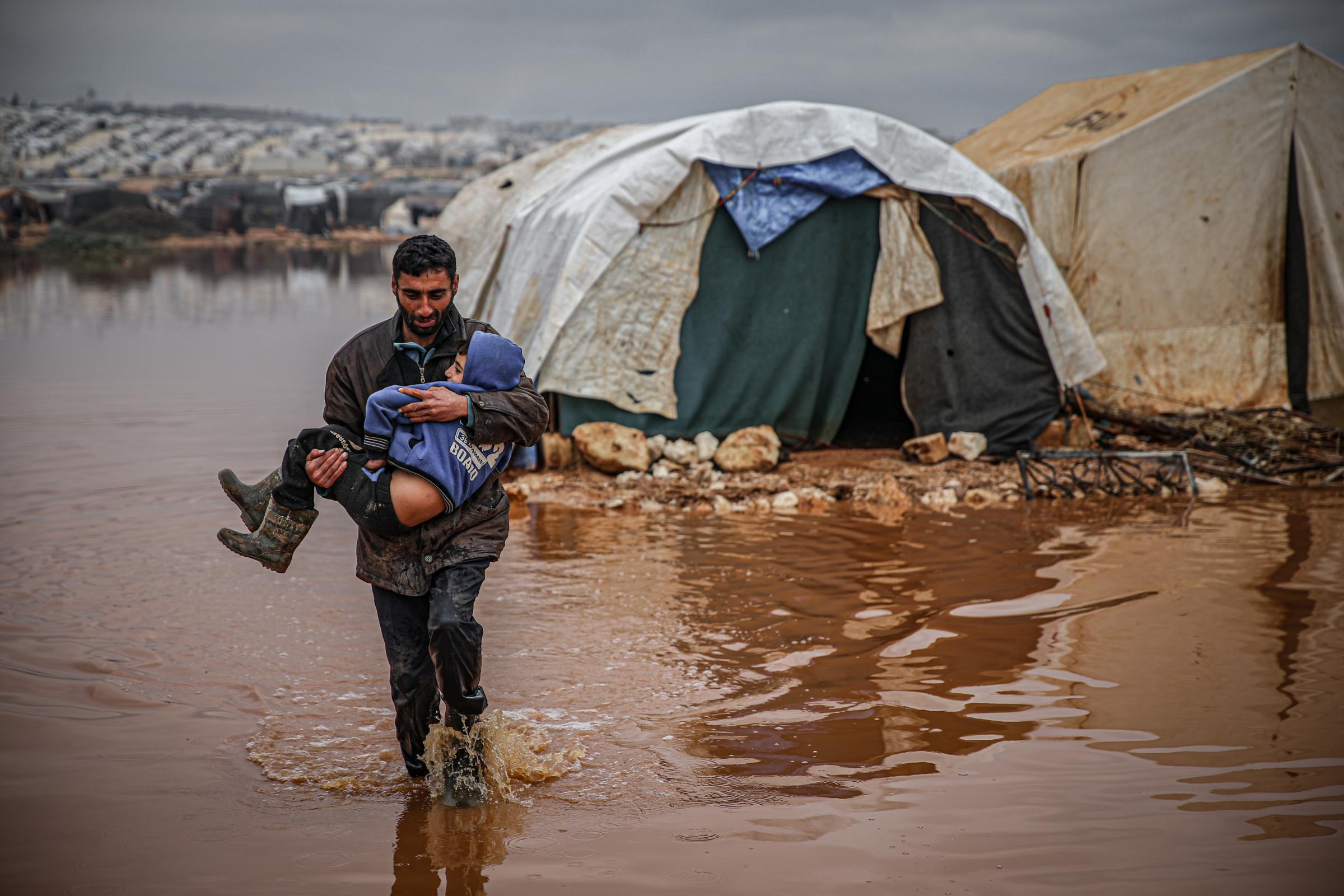 IDLIB, SYRIA - JANUARY 19: Syrian civilian carries a child as they evacuate their belongings from flooded tents at the Kefer Lusin refugee camp after heavy rain caused floods in Idlib, Syria on January 19, 2021. Civilians, who fled the attacks of Assad Re