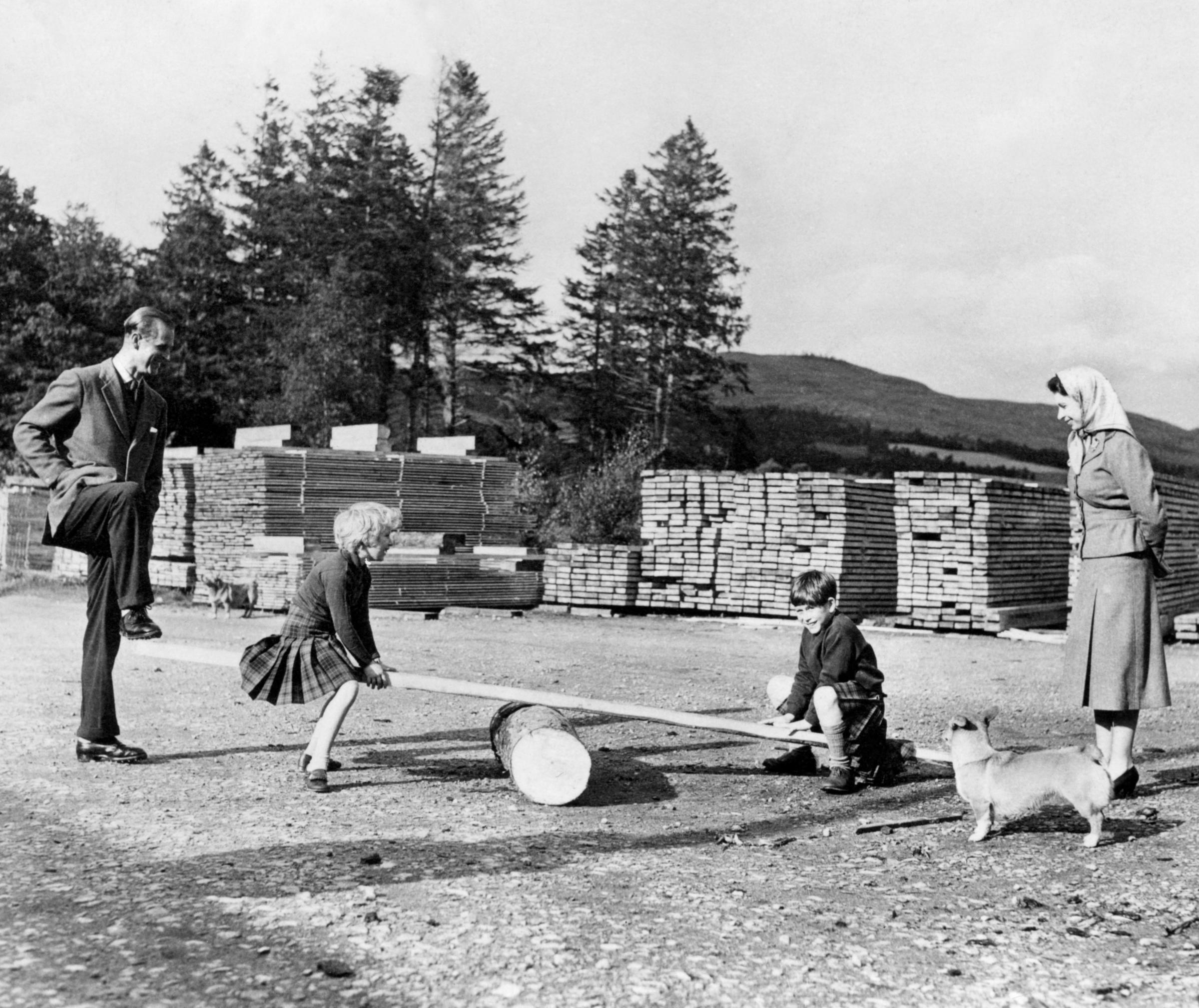 The Prince of Wales with his sister Princess Anne, watched closely by their parents, Queen Elizabeth II and the Duke of Edinburgh, playing on a see-saw made from a log and a plank of wood with the help of their father on the Balmoral Estate.