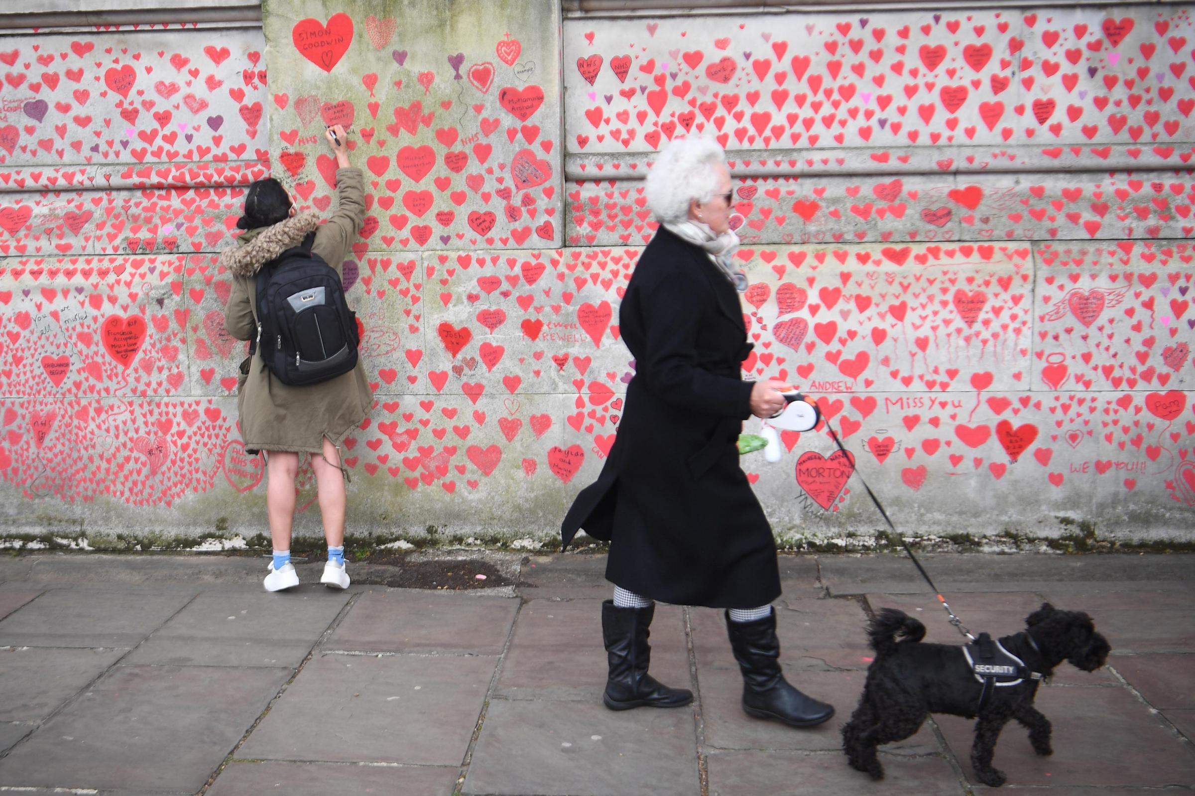 A woman writes in a heart on the National Covid Memorial Wall on the Embankment in London