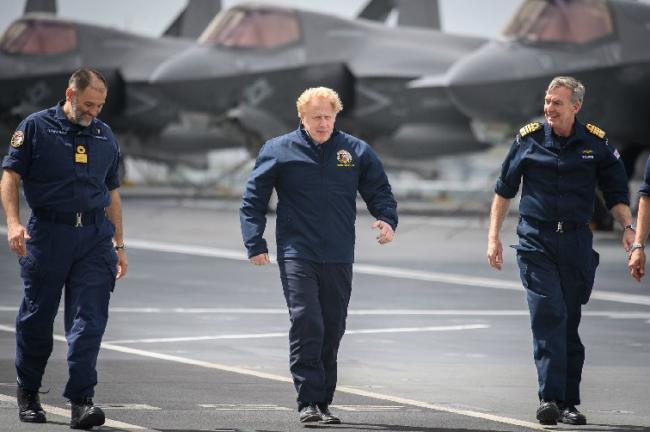 (Left to right) Commodore Steve Moorhouse, Prime Minister Boris Johnson and First Sea Lord Admiral Tony Radakin face strong winds as they walk on the HMS Queen Elizabeth II aircraft carrier.