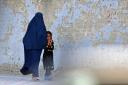 A burqa-clad woman walks with a girl along a street in Kabul