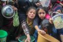 Children queue for food that is cooked in large pots and distributed for free on December 28, 2023 in Rafah, Gaza.