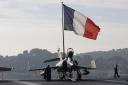 Flight deck crew work around a Super Etendard fighter jet as a French flag flies aboard the French nuclear-powered aircraft carrier Charles de Gaulle before its departure from the naval base of Toulon, France, November 18, 2015. France's Charles de Gaulle