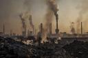 INNER MONGOLIA, CHINA - NOVEMBER 04: Smoke billows from a large steel plant as a Chinese labourer works at an unauthorized steel factory, foreground, on November 4, 2016 in Inner Mongolia, China. To meet China's targets to slash emissions of carbon