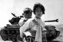 Carrying her baby brother on her back, a war weary Korean girl walks by a stalled tank, at Haengju, Korea, in 1951 during the height of the conflict.