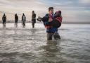 A migrant carries a child with people-smugglers behind him as he hurries to board a boat on a beach near Dunkirk in an attempt to cross the Channel