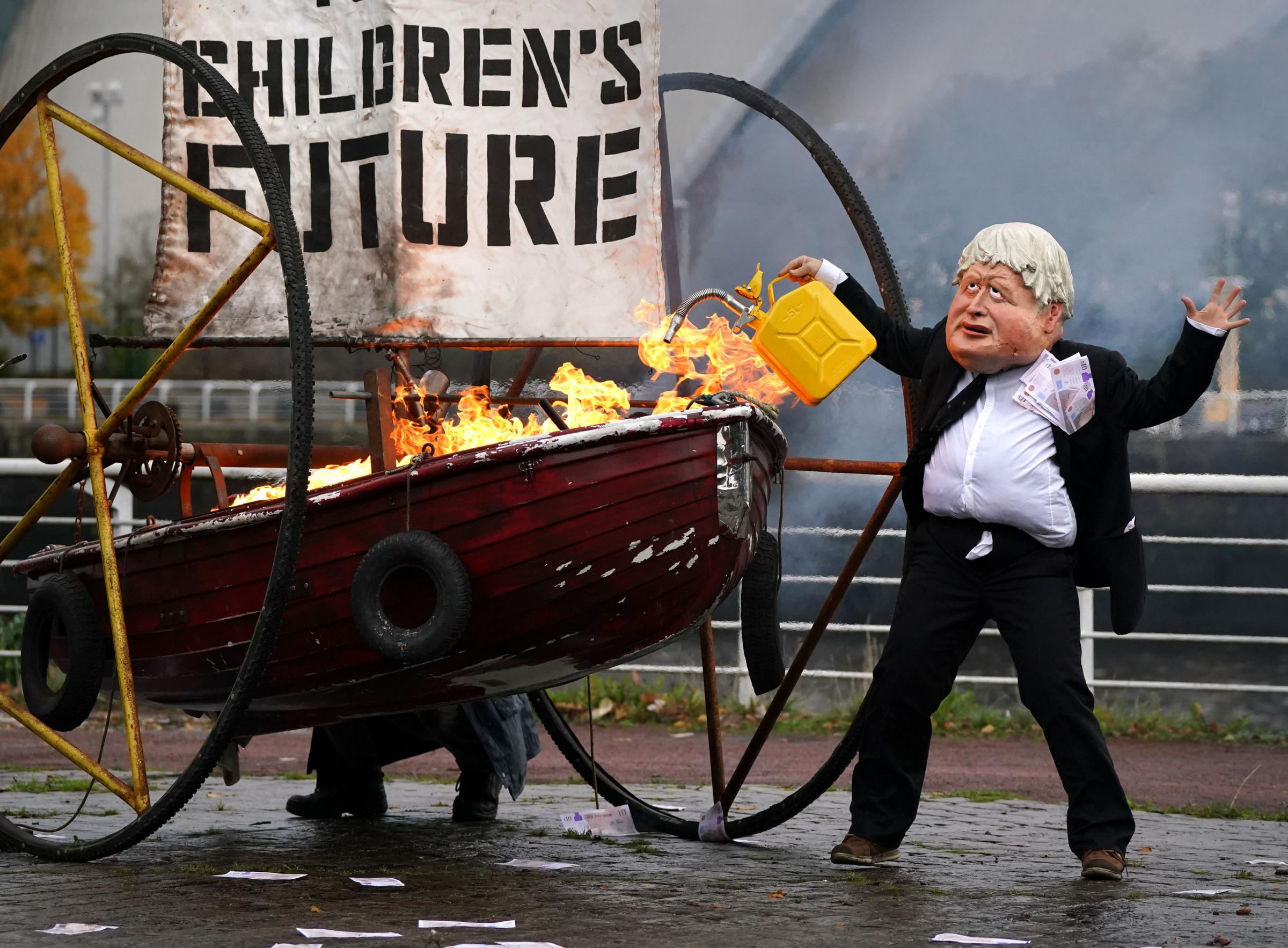 One of the many protests ahead of COP26. Performers from Ocean Rebellion dressed as Prime Minister Boris Johnson and an Oilhead set light to the sail of a small boat which reads Your Childrens Future as they burn stacks of money on the banks of the