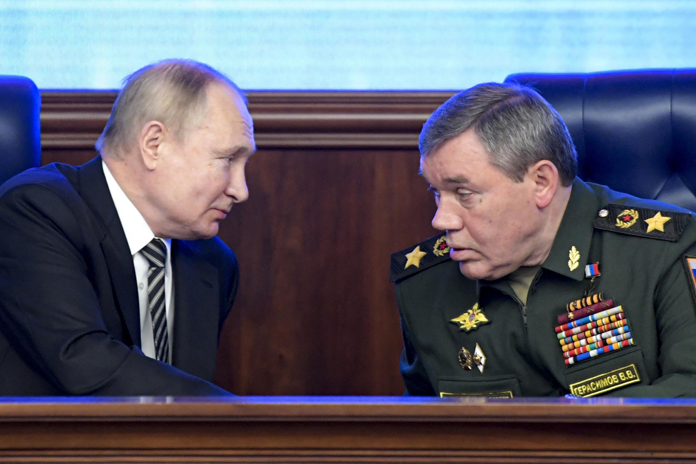Russian President Vladimir Put, left, and Russian General Staff Valery Gerasimov talk to each other during an extended meeting of the Russian Defense Ministry Board at the National Defense Control Center with a Russian military map showing the alleged