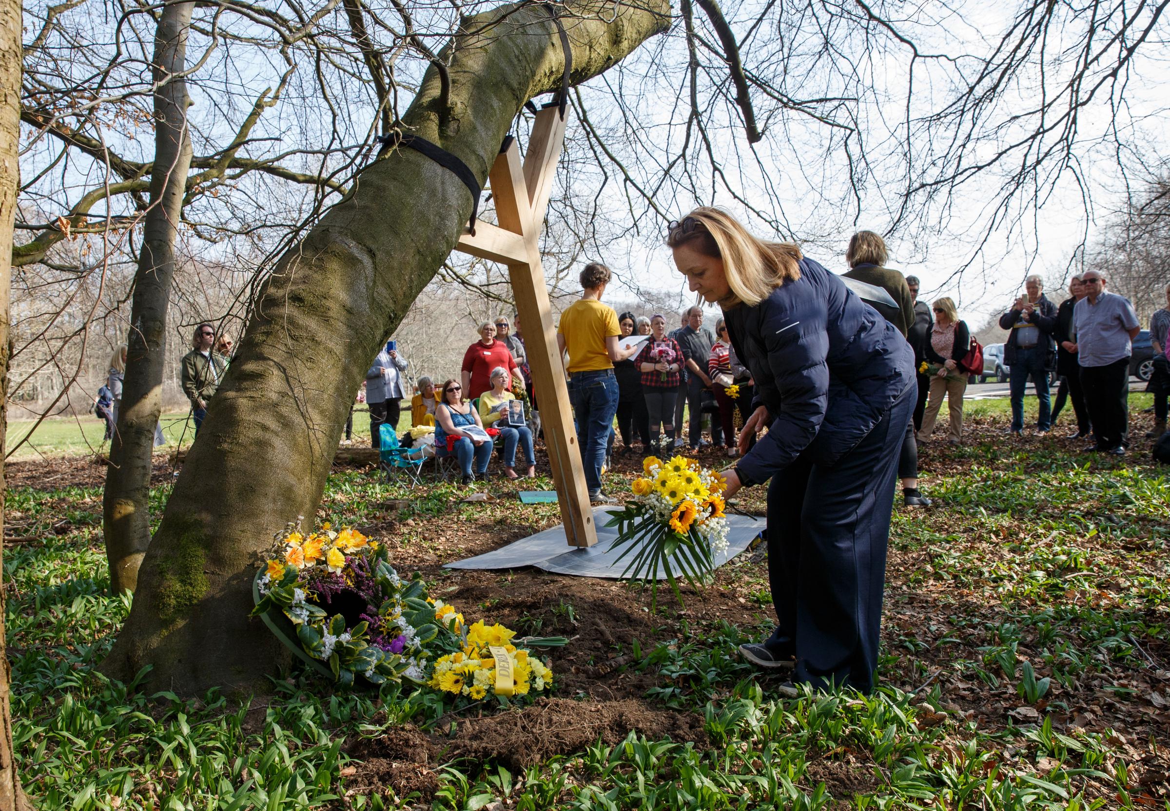 People place bouquets of flowers next to a tree at Pollok Country park, Glasgow on the second anniversary of the first Covid lockdown. Next to the floral tributes is the first of a series of wooden tree supports created by The Heralds covid memorial