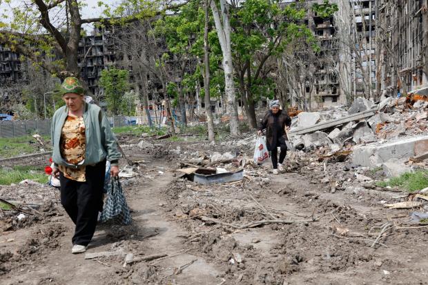 HeraldScotland: Women walk past a destroyed apartment building in Mariupol (Alexei Alexandrov/AP)
