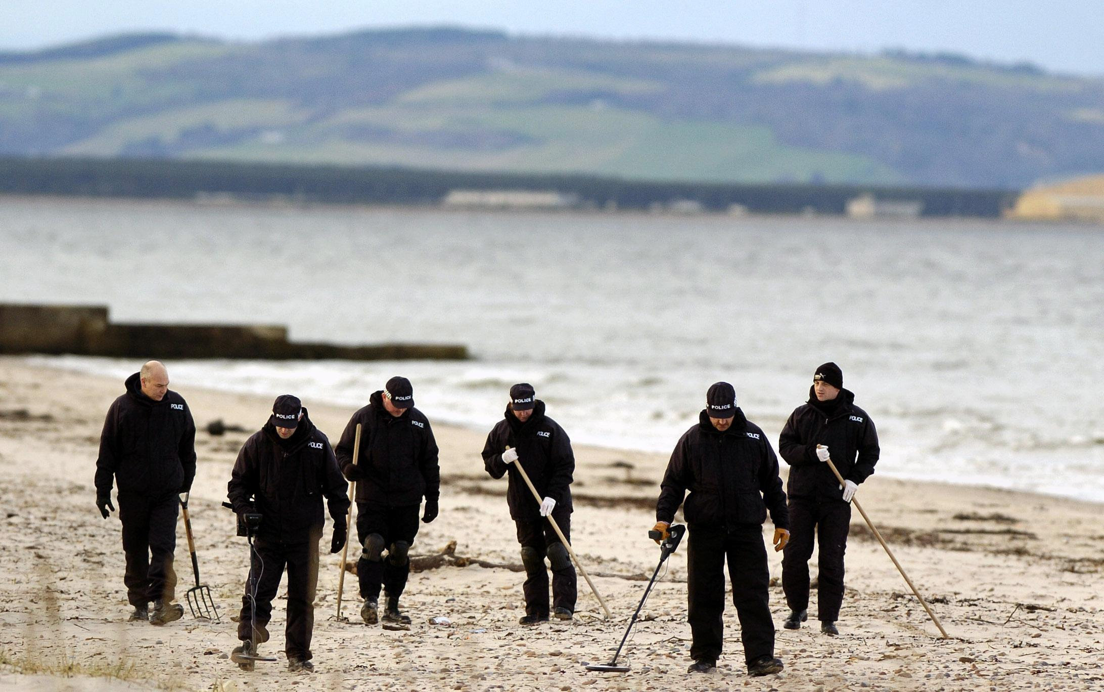 Police officers search Nairn beach, near Inverness, Scotland using metal detectors.
