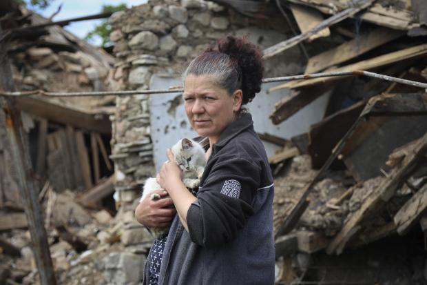 A woman stands next to a destroyed house in Mariupol, in territory under the government of the Donetsk People's Republic, eastern Ukraine, Tuesday, May 17, 2022. (AP Photo/Alexei Alexandrov)