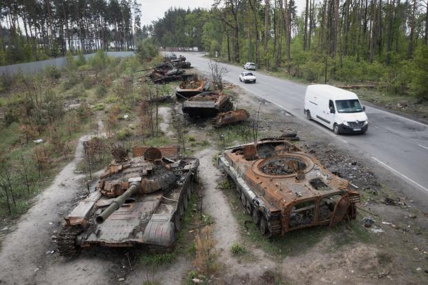 Cars pass by destroyed Russian tanks in a recent battle against Ukrainians in the village of Dmytrivka, close to Kyiv, Ukraine, Monday, May 23, 2022. No matter where Ukrainians live, the 3-month-old war never seems to be far away. Those in towns and