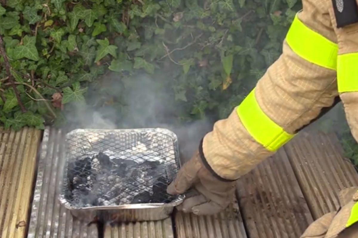 A disposable barbecue is attended to by a member of the fire service