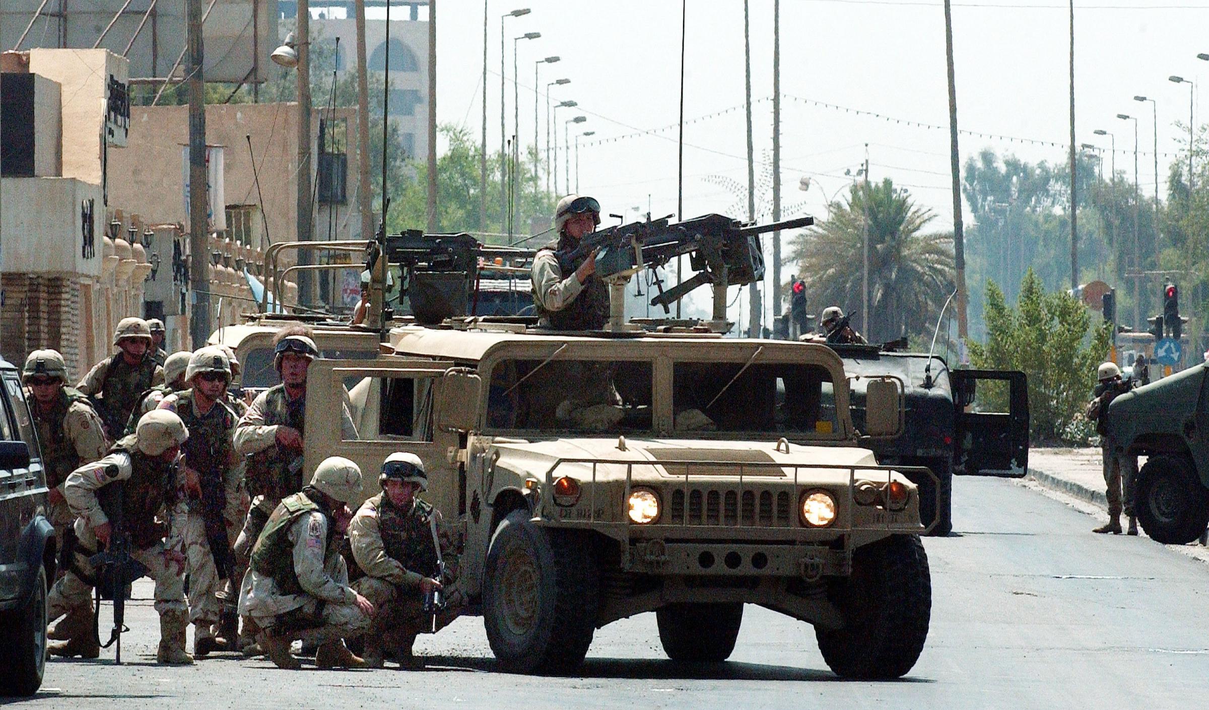 BAGHDAD, IRAQ - AUGUST 7: U.S. Army troops with the 82nd Airborne take cover behind a humvee during a gun battle after a rocket propelled grenade (RPG) attack on U.S. troops August 7, 2003 in dowtown Baghdad, Iraq. At least two U.S. soldiers were