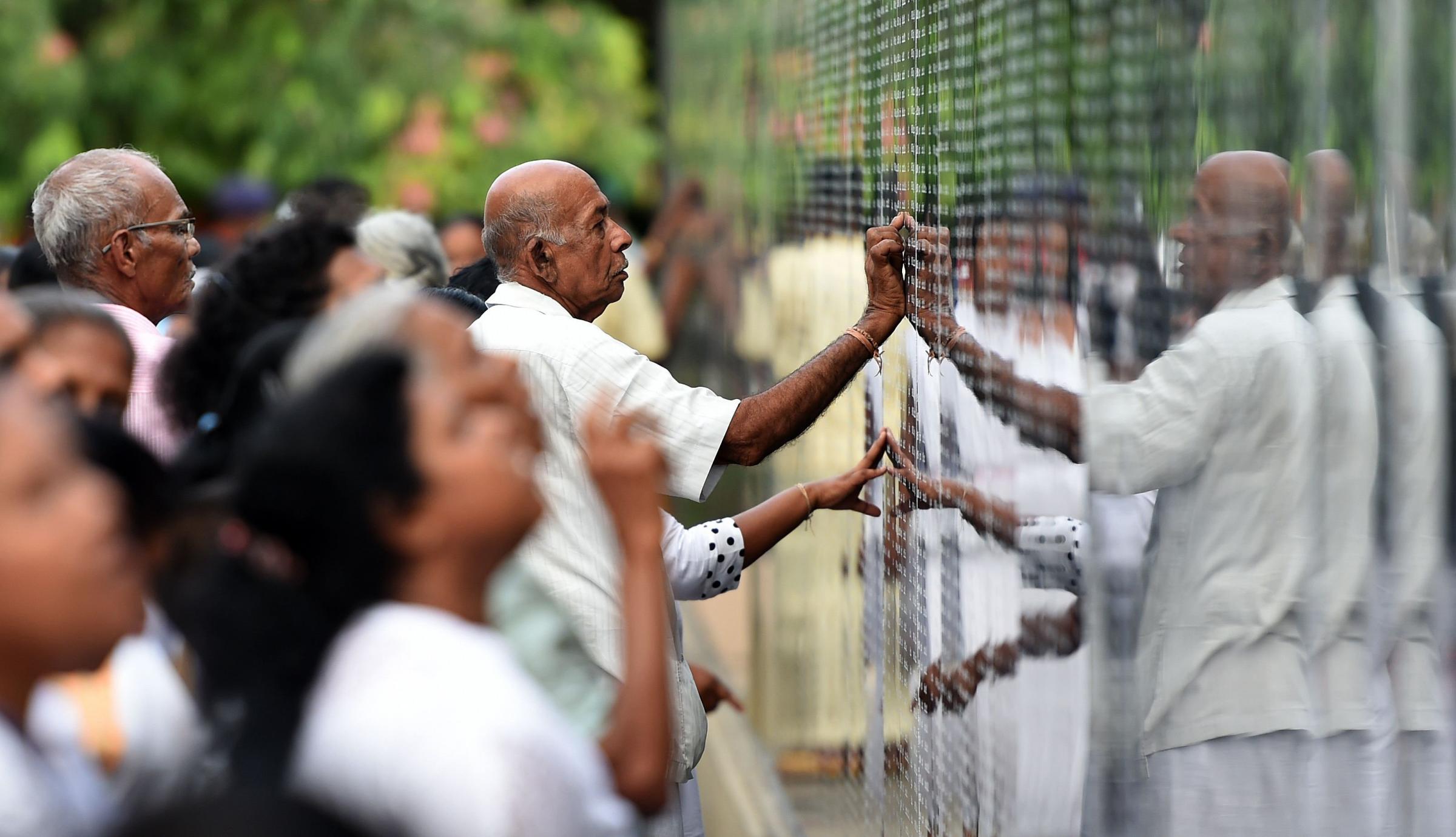 Sri Lankan attendees read through names of fallen soldiers on a memorial for those who died in the decades-long conflict against the Tamil Tigers, during a commemorative ceremony marking the 9th anniversary of the end of the islands civil war, in the