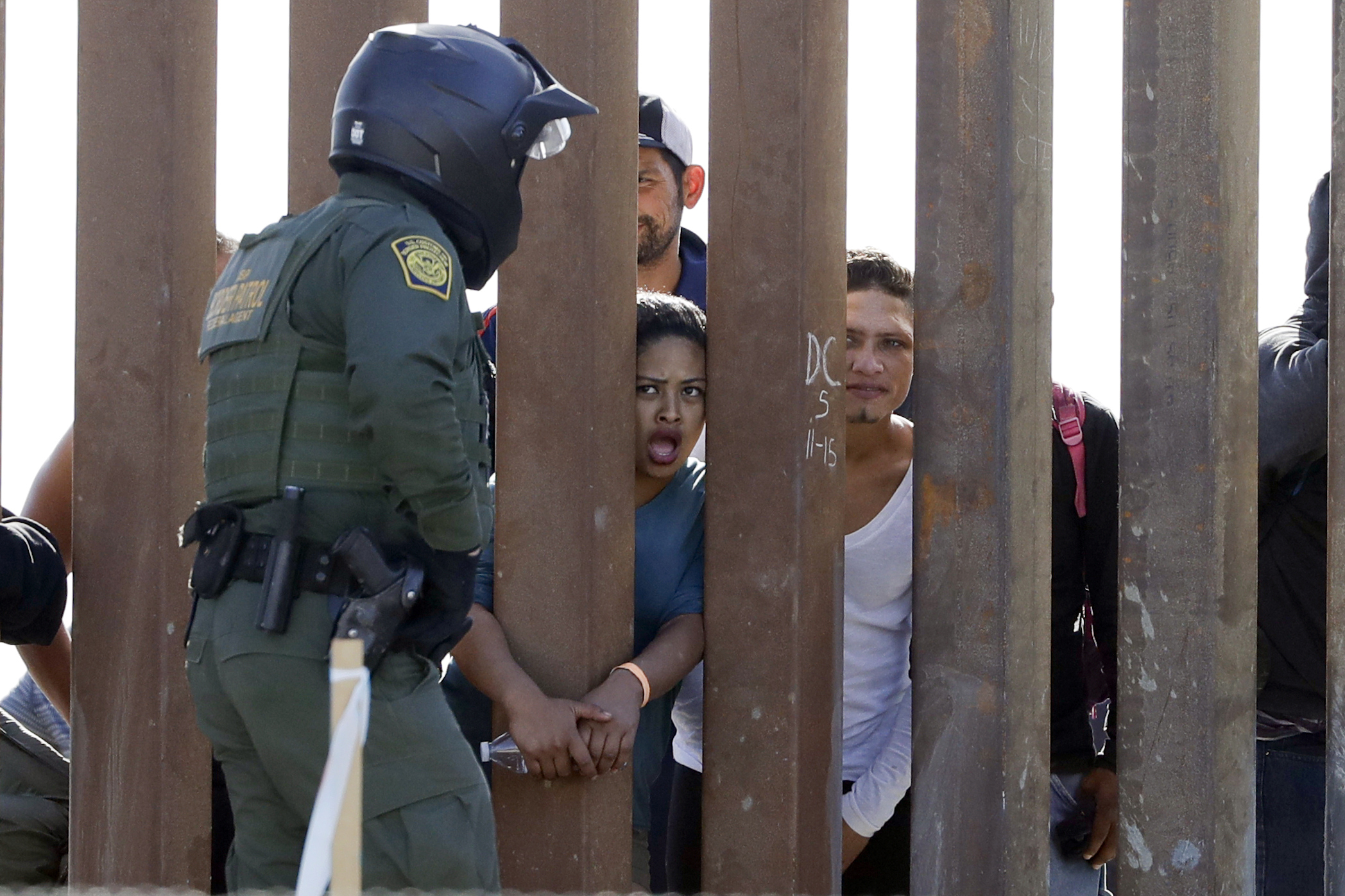 Migrants from Central America yell through a border wall at a U.S. Border Patrol agent after he pulled down a banner Sunday, Nov. 25, 2018, in San Diego. Migrants approaching the U.S. border from Mexico were enveloped with tear gas Sunday after a few
