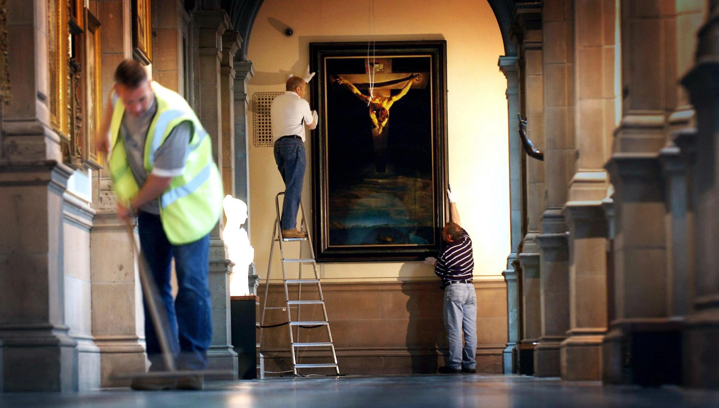 In this posed photograph workers hang Salvador Dalis Christ Of St John Of The Cross at Kelvingrove Art Gallery and Museum in Glasgow. The painting has been returned to its original home to mark the reopening of Kelvingrove on July 11 following a