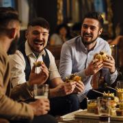 Three men are sitting together in a bar/restaurant lounge. They are laughing and talkig while enjoying burgers and beer..