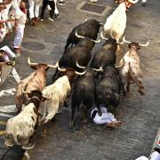 A runner falls as people run through the street with fighting bulls at the San Fermin Festival in Pamplona, northern Spain, Friday, July 8, 2022. Revellers from around the world flock to the city every year for nine days of uninterrupted partying in