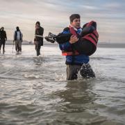 A migrant carries a child with people-smugglers behind him as he hurries to board a boat on a beach near Dunkirk in an attempt to cross the Channel