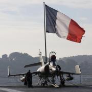 Flight deck crew work around a Super Etendard fighter jet as a French flag flies aboard the French nuclear-powered aircraft carrier Charles de Gaulle before its departure from the naval base of Toulon, France, November 18, 2015. France's Charles de