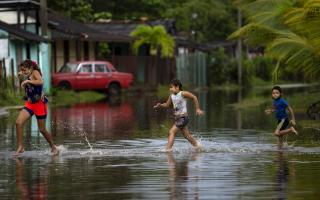 Children run in a flooded street caused by rains brought on by Hurricane Ida, in Guanimar, Artemisa province, Cuba, Saturday Aug. 28, 2021. (AP Photo/Ramon Espinosa).